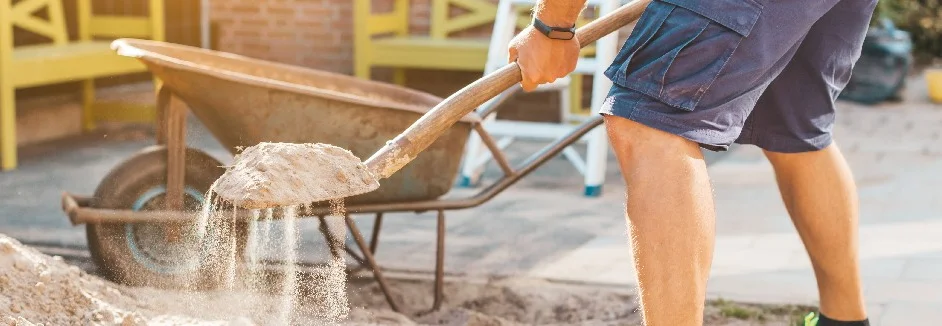 Person schaufelt Sand in Schubkarre